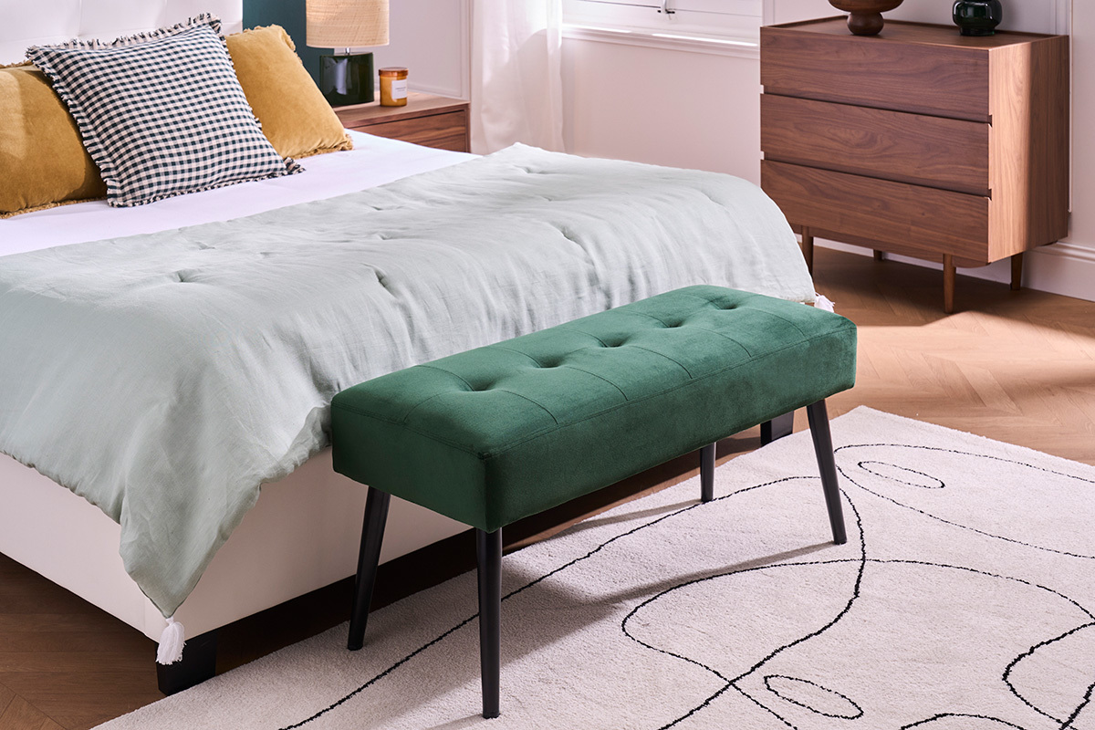 Banc capitonn� vert fonc� en velours et m�tal noir au pied d'un lit.