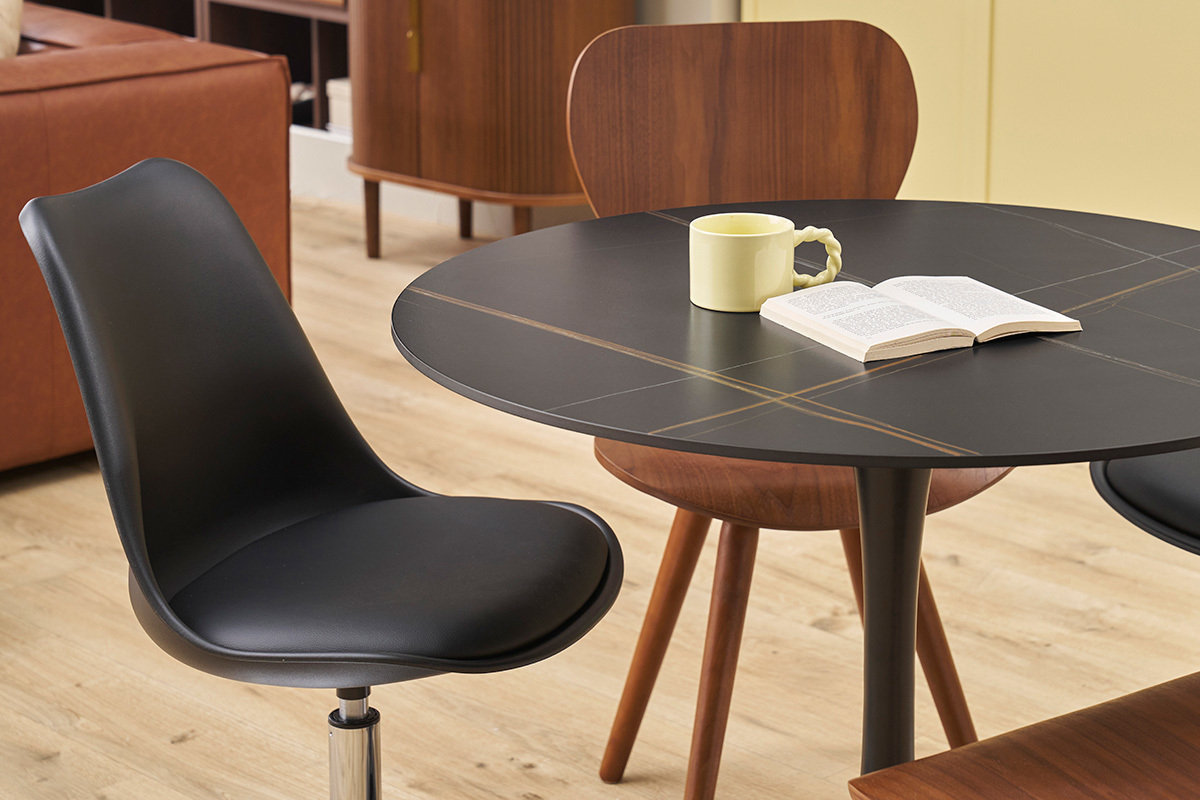 Chaise pivotante noire STEEVY V2 pr�s d'une table, vue partielle.