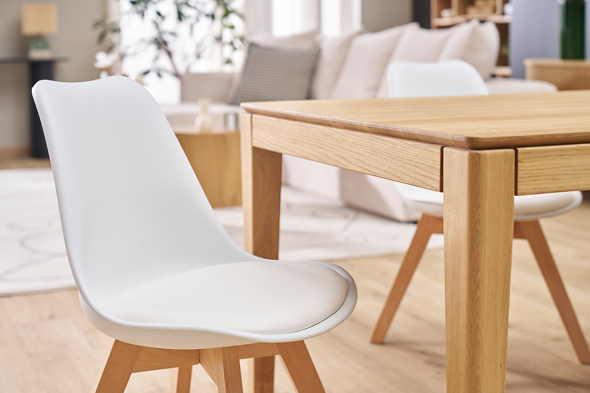 Chaises blanches avec pieds en bois clair autour d'une table en bois.