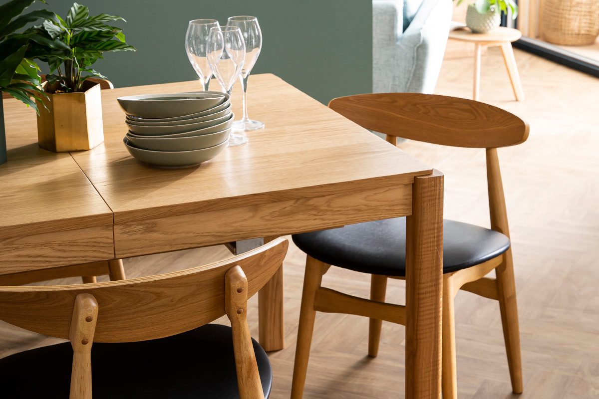 Chaises scandinaves en bois clair et assises noires autour d'une table en bois.