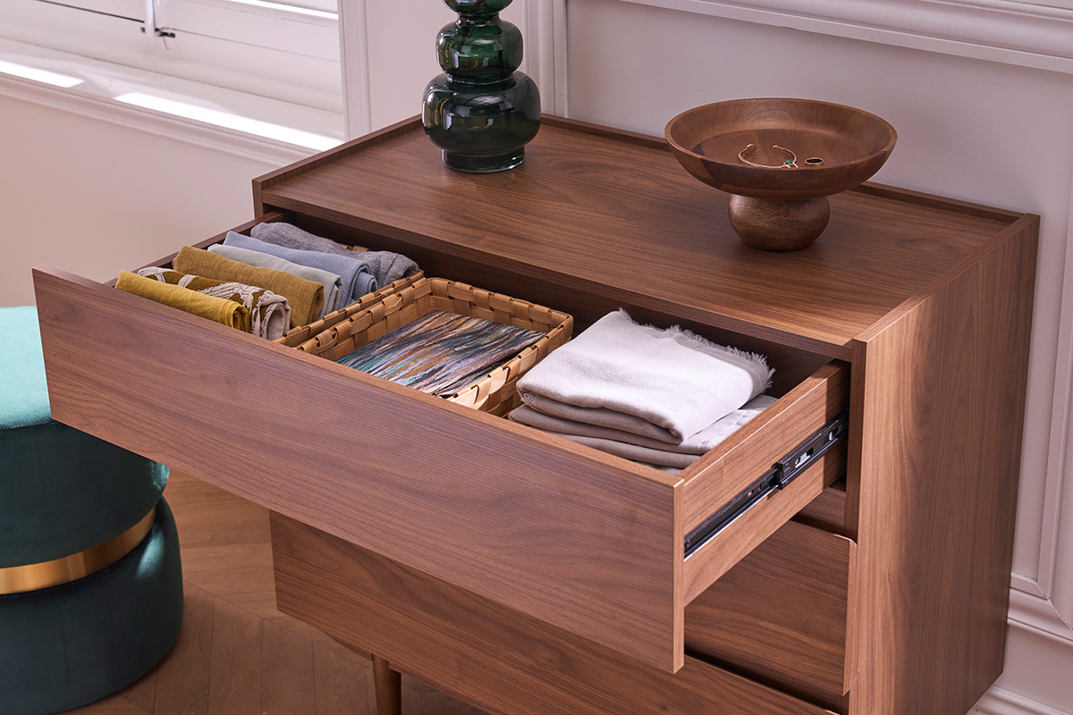 Commode SANAA en bois fonc�, premier tiroir ouvert, contenant des v�tements et un panier.