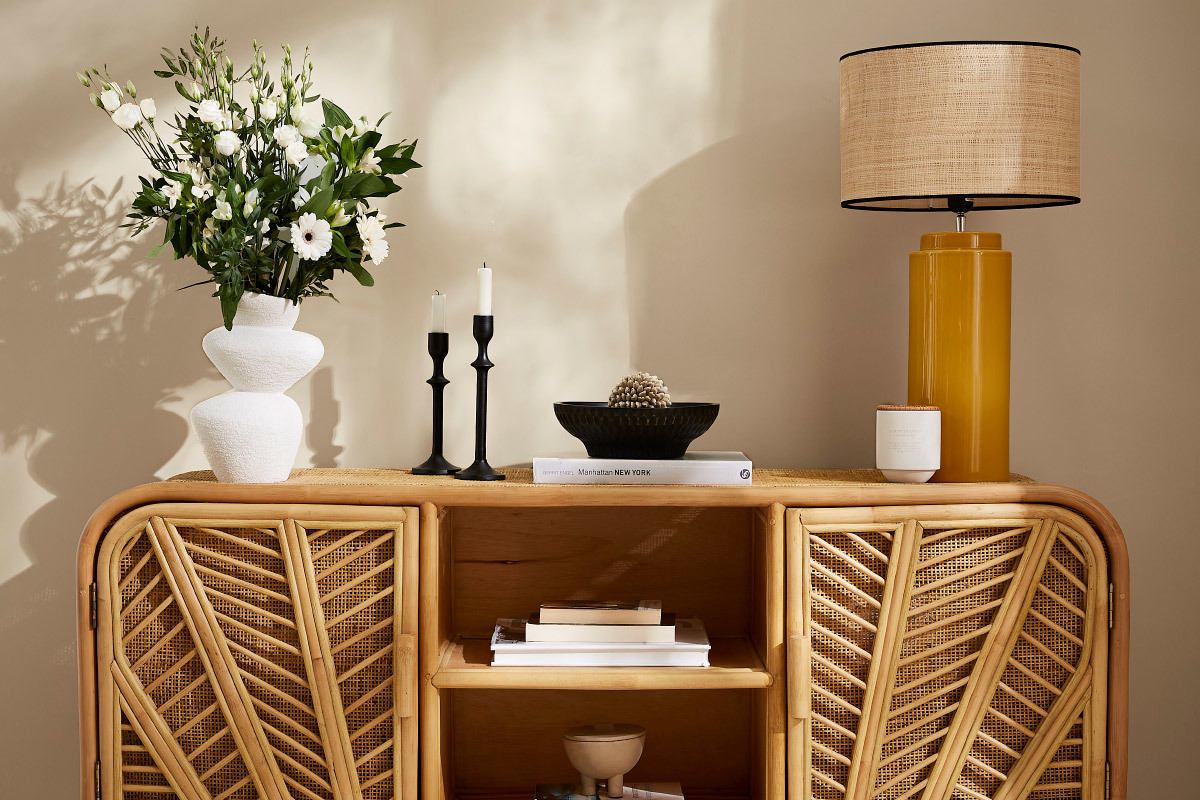 Lampe jaune en c�ramique avec abat-jour en raphia sur buffet, � c�t� de d�corations.