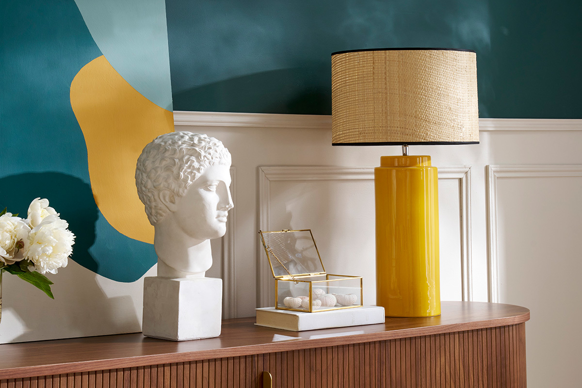 Lampe en c�ramique jaune avec abat-jour en raphia sur un buffet en bois.