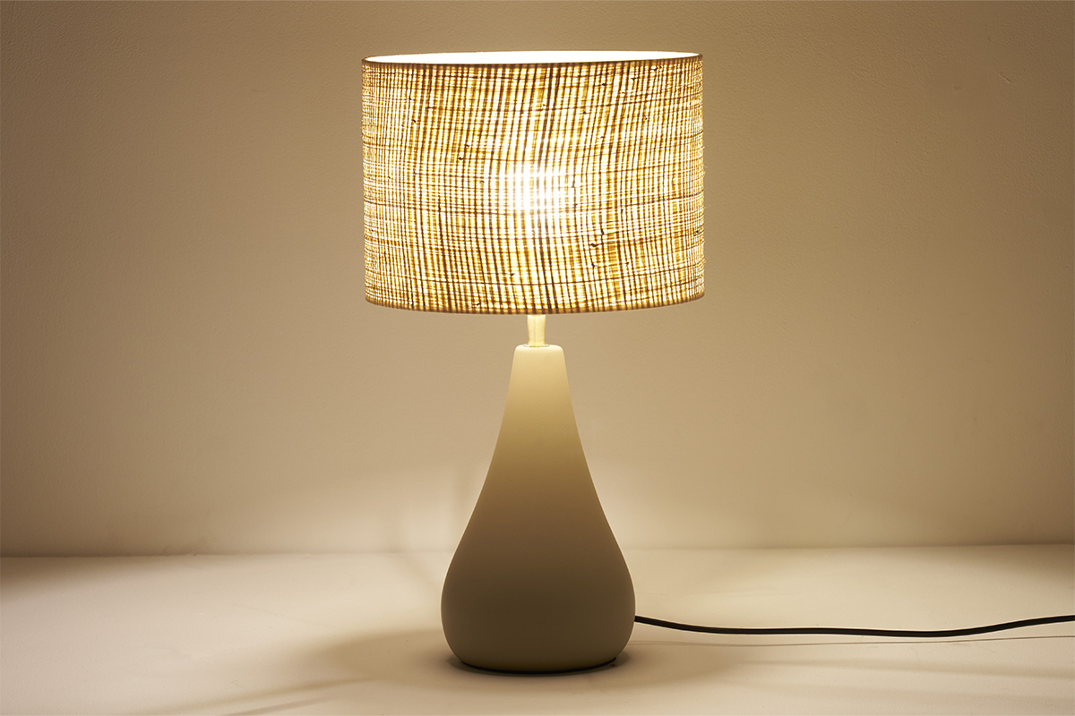 Lampe � poser taupe en c�ramique avec abat-jour en raphia allum�e, vue de face.