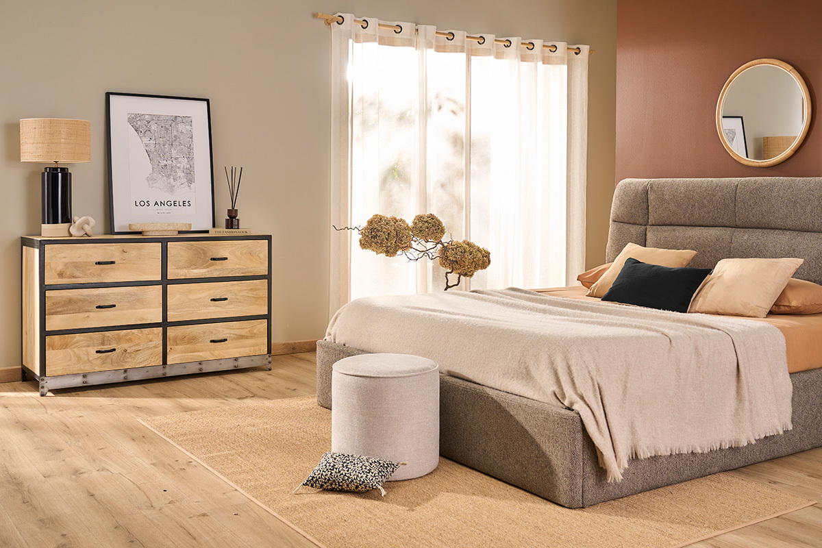 Pouf rond beige en tissu effet velours devant un lit dans une chambre moderne.