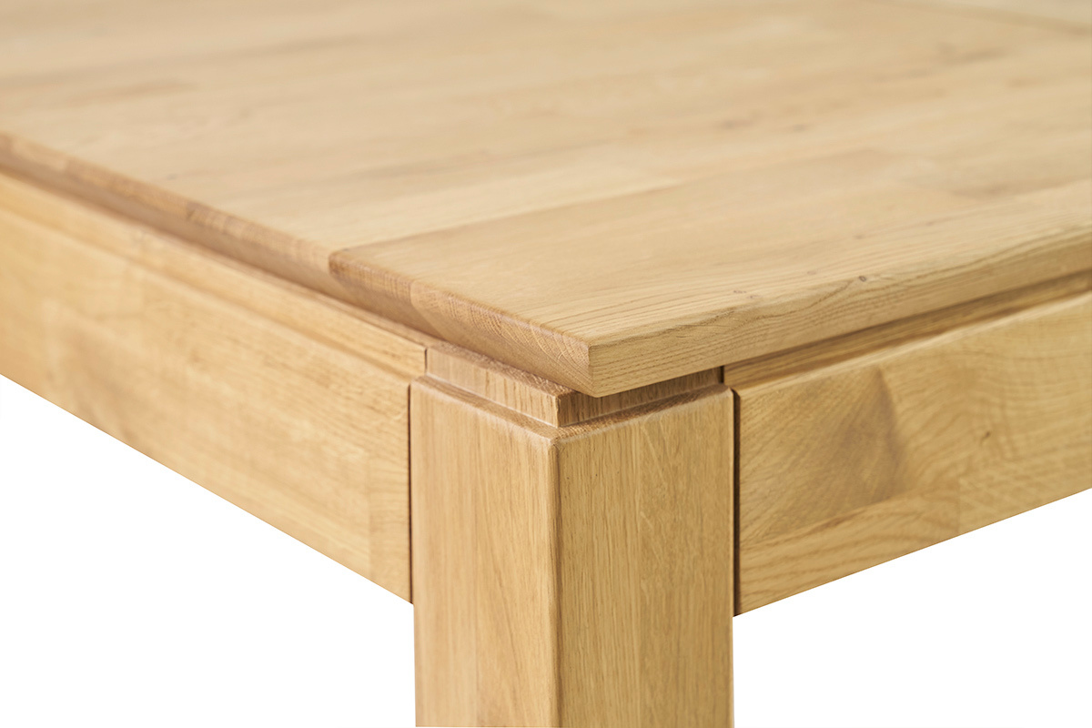 D�tail de coin d'une table � manger en bois clair, plateau et pied visibles.