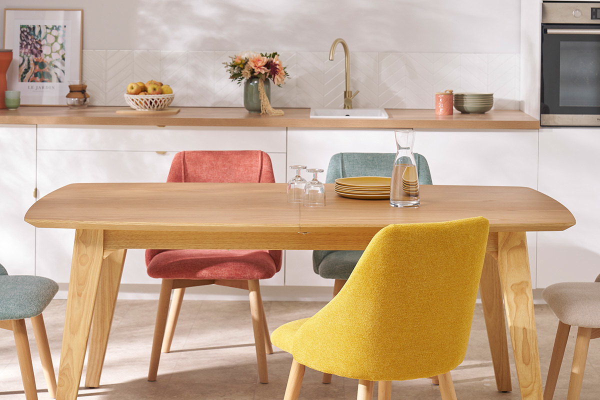 Table FIFTIES en bois clair avec rallonges int�gr�es, vue de face, entour�e de chaises color�es.
